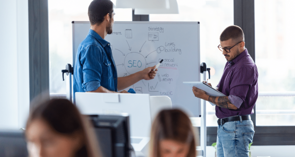 Two professionals discussing SEO strategies in front of a whiteboard.