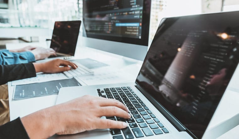 Web developers coding and collaborating on laptops and desktops in a modern office.